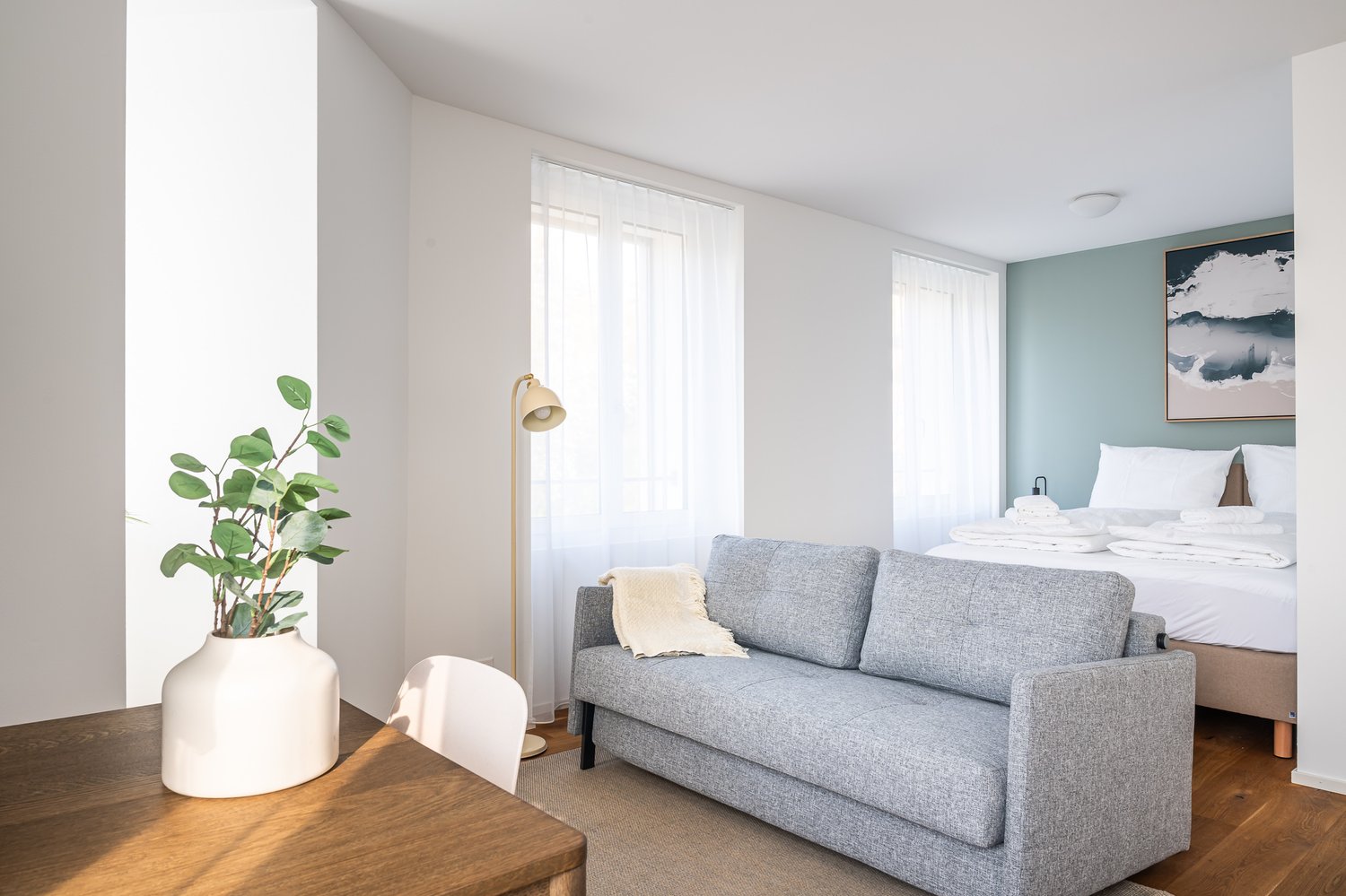 A small room with a bed, a couch, a table, a plant, and a lamp.