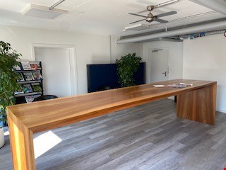 Spacious office with hardwood-style flooring, large wooden desk, ceiling fan, and a balcony or terrace visible through the window.
