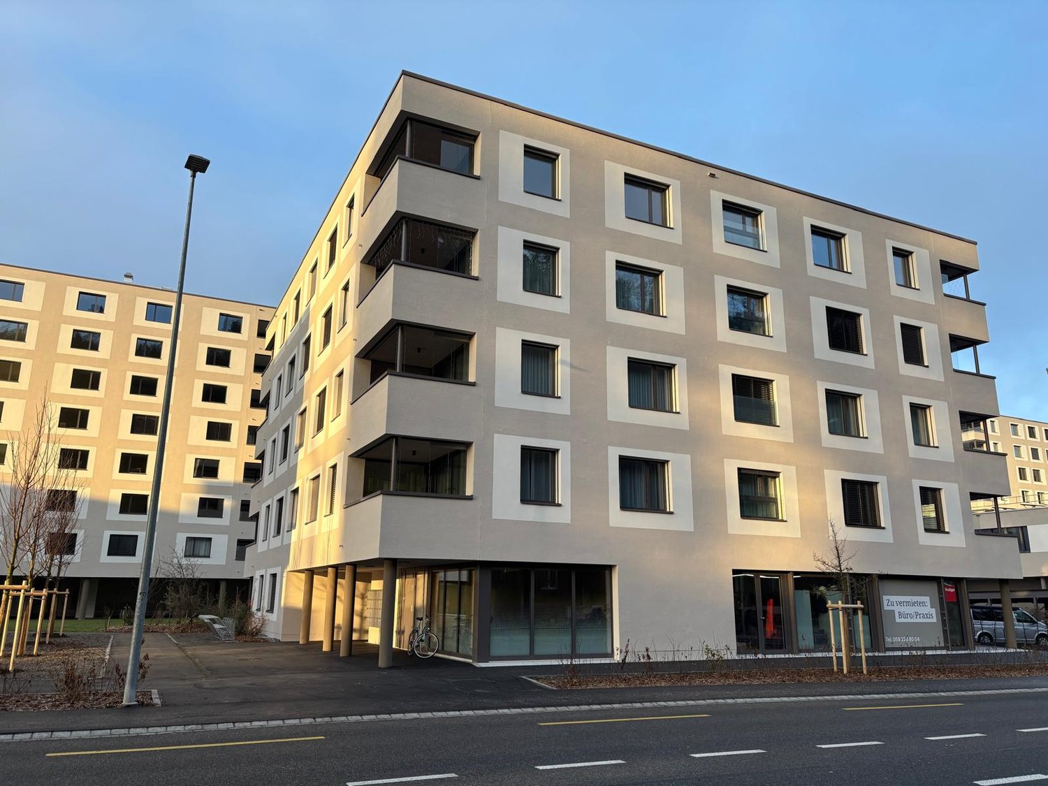 An apartment building with 4 stories, white exterior with large windows, balconies on upper floors, bike parked near entrance