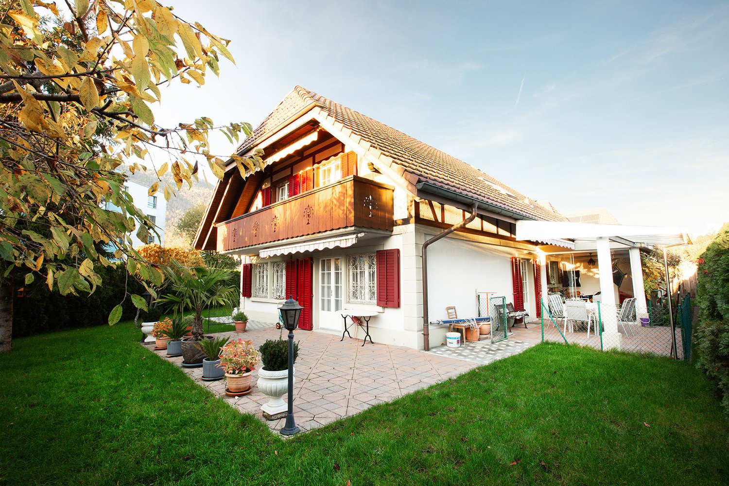 white house, brown roof, red shutters, balcony, patio, garden, lawn, trees