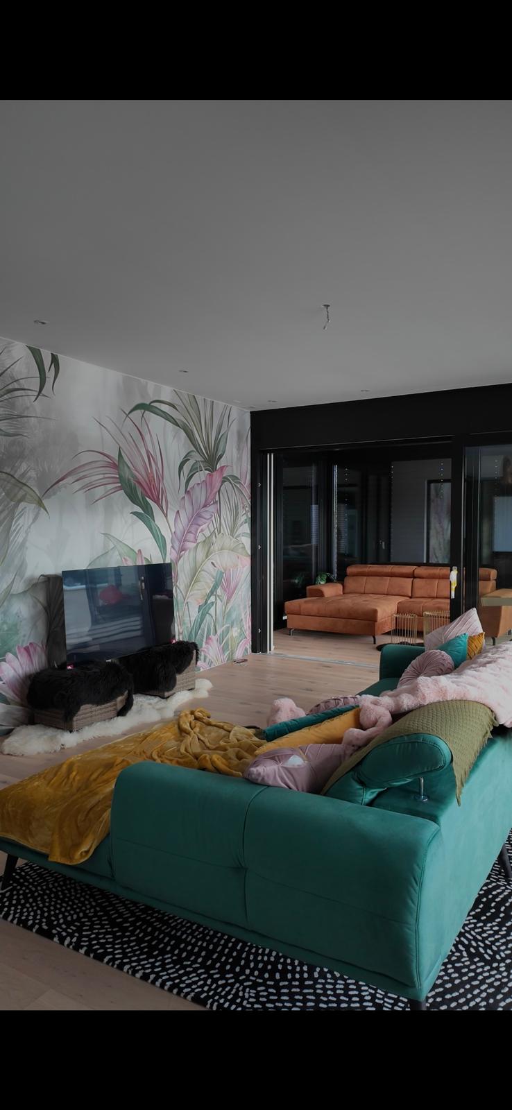 living room with large glass windows and balcony, wooden floor, teal sofa with cushions, coffee table, and wall mural, TV, and a rug