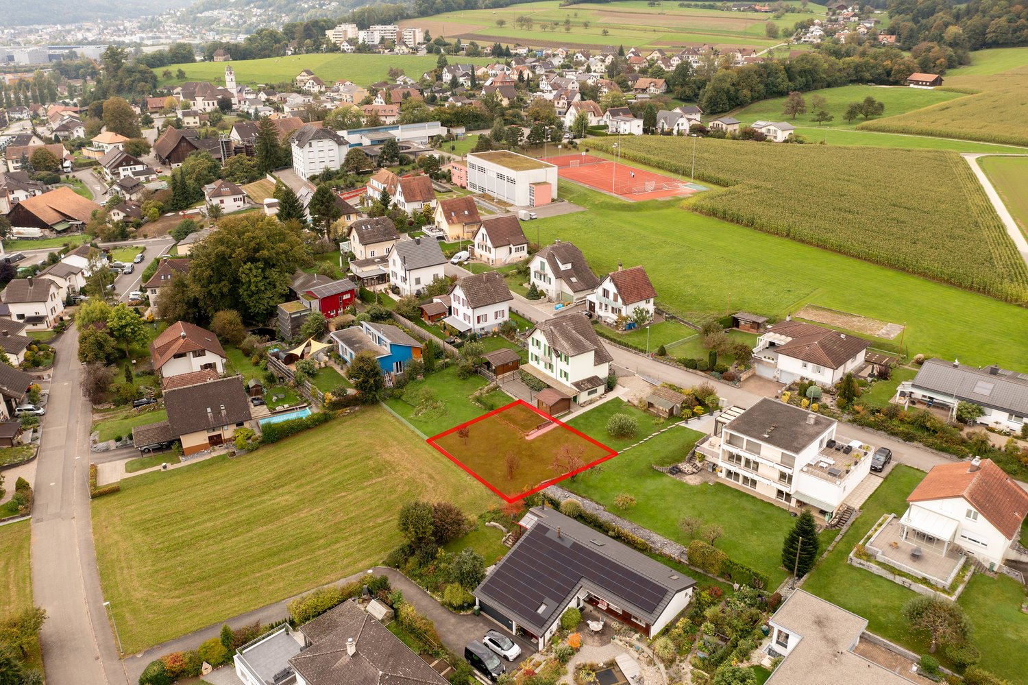 Suburban neighborhood with various sized houses, one empty plot marked with red rectangle, houses have various features like garages and solar panels