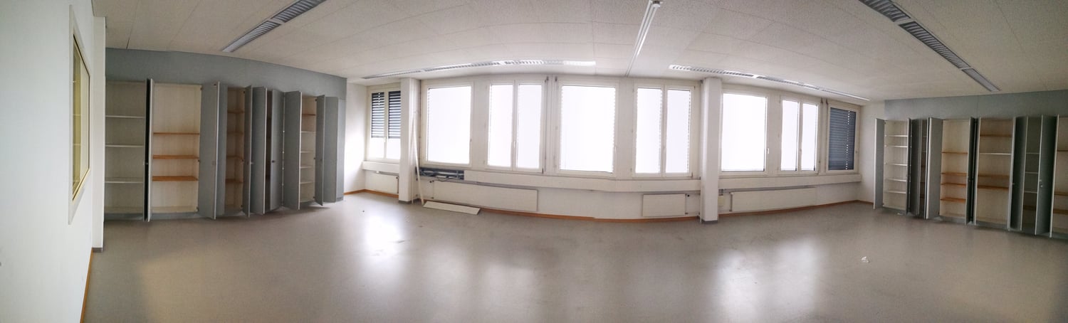 Large open office space with multiple windows, built-in shelving units, and a curved seating area along the wall.