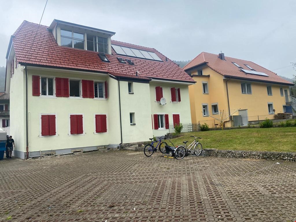 Two-story house with red roofs and windows, solar panels, brick driveway, bicycles parked