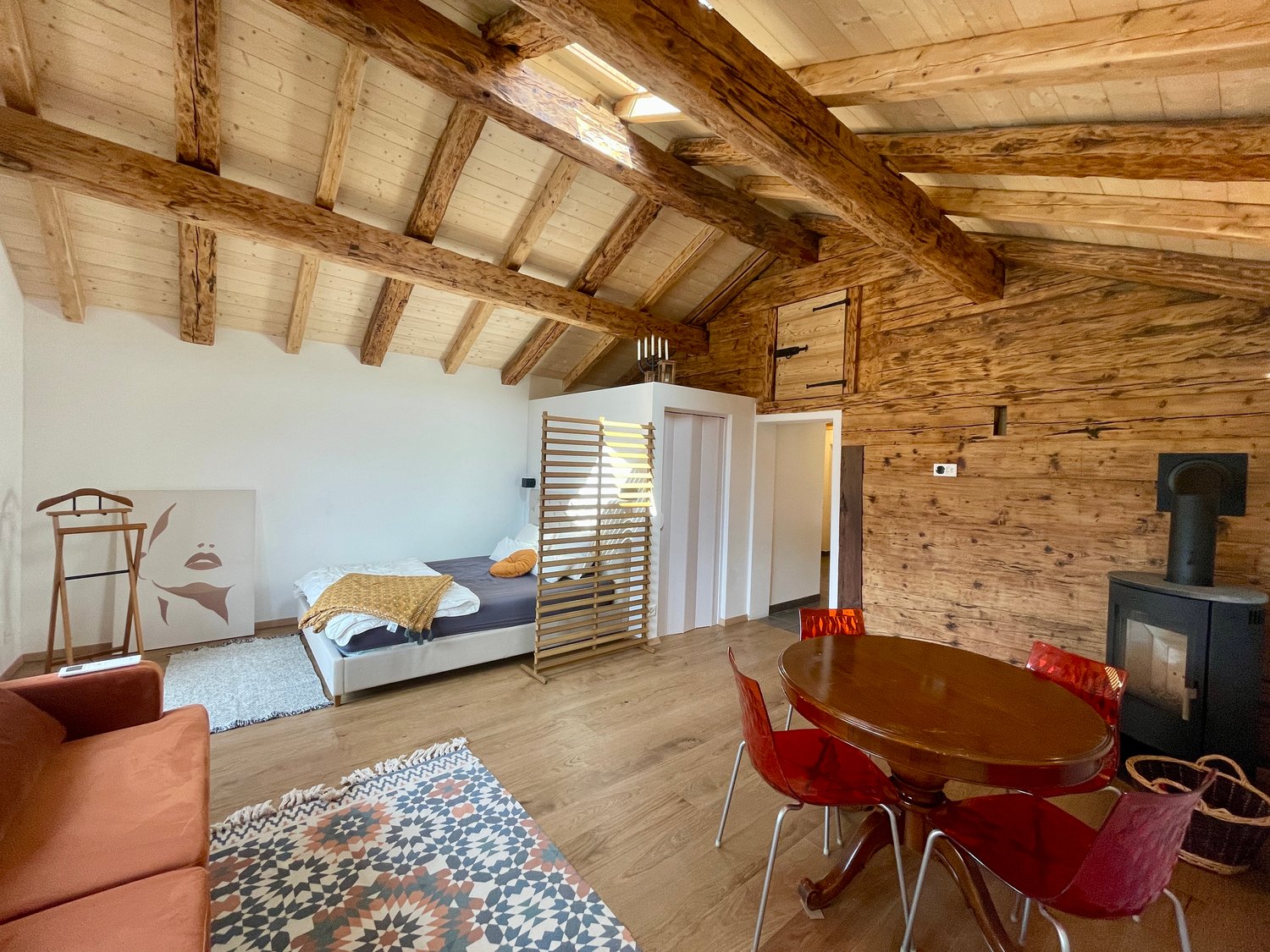 Exposed wooden beams, fireplace, bedroom with bed, wooden table with red chairs, carpet, couch