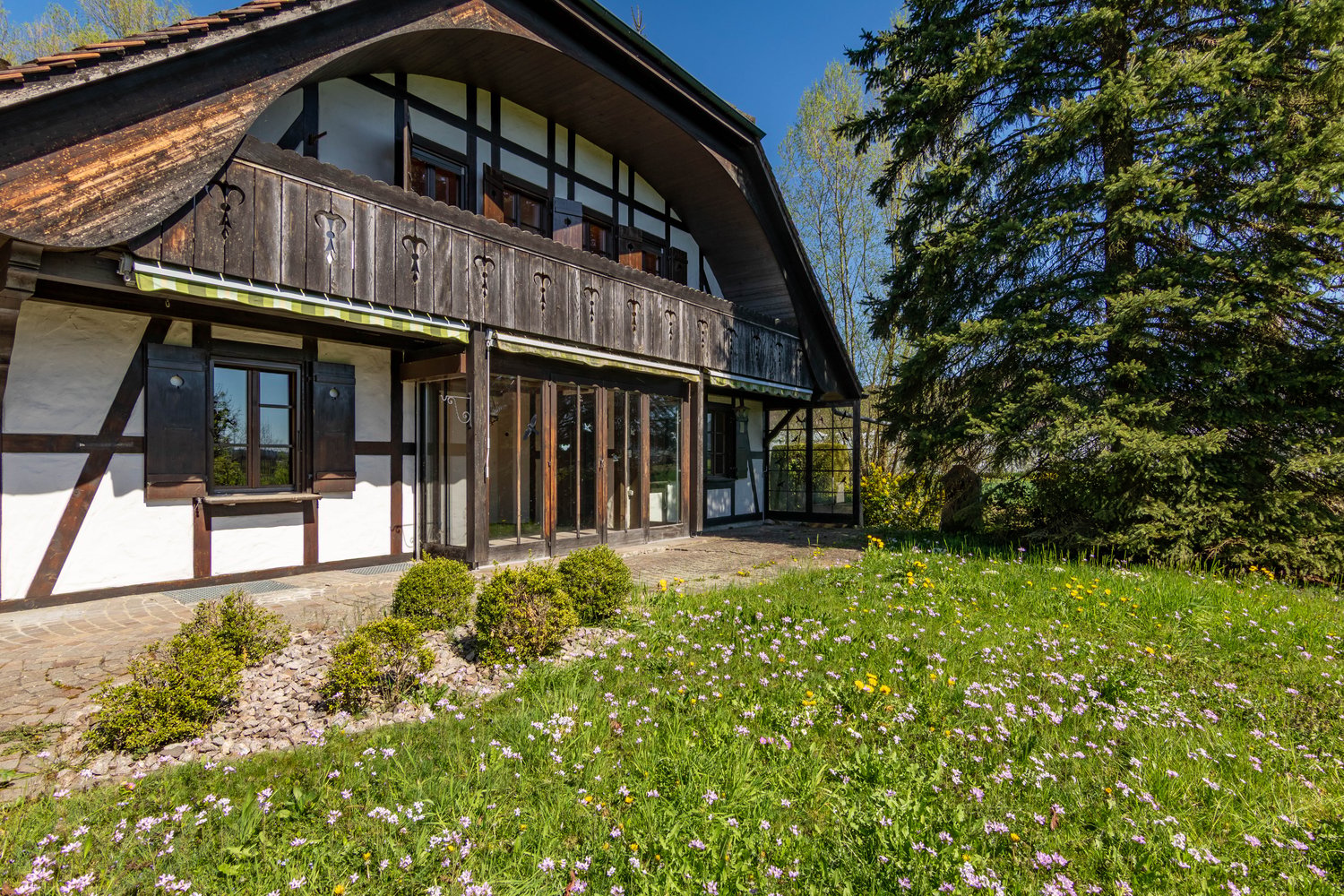 Traditional house, wooden exterior, white walls, wooden balcony, glass doors, large windows, surrounded by greenery