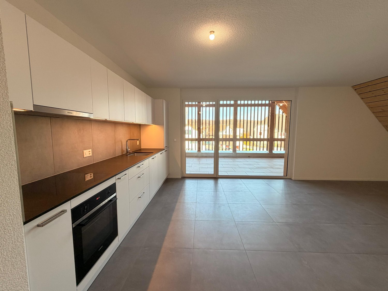 modern kitchen with white cabinets, wooden floors, gray countertops, built-in oven, sink with faucet, sliding glass doors to the terrace, white walls, recessed lighting