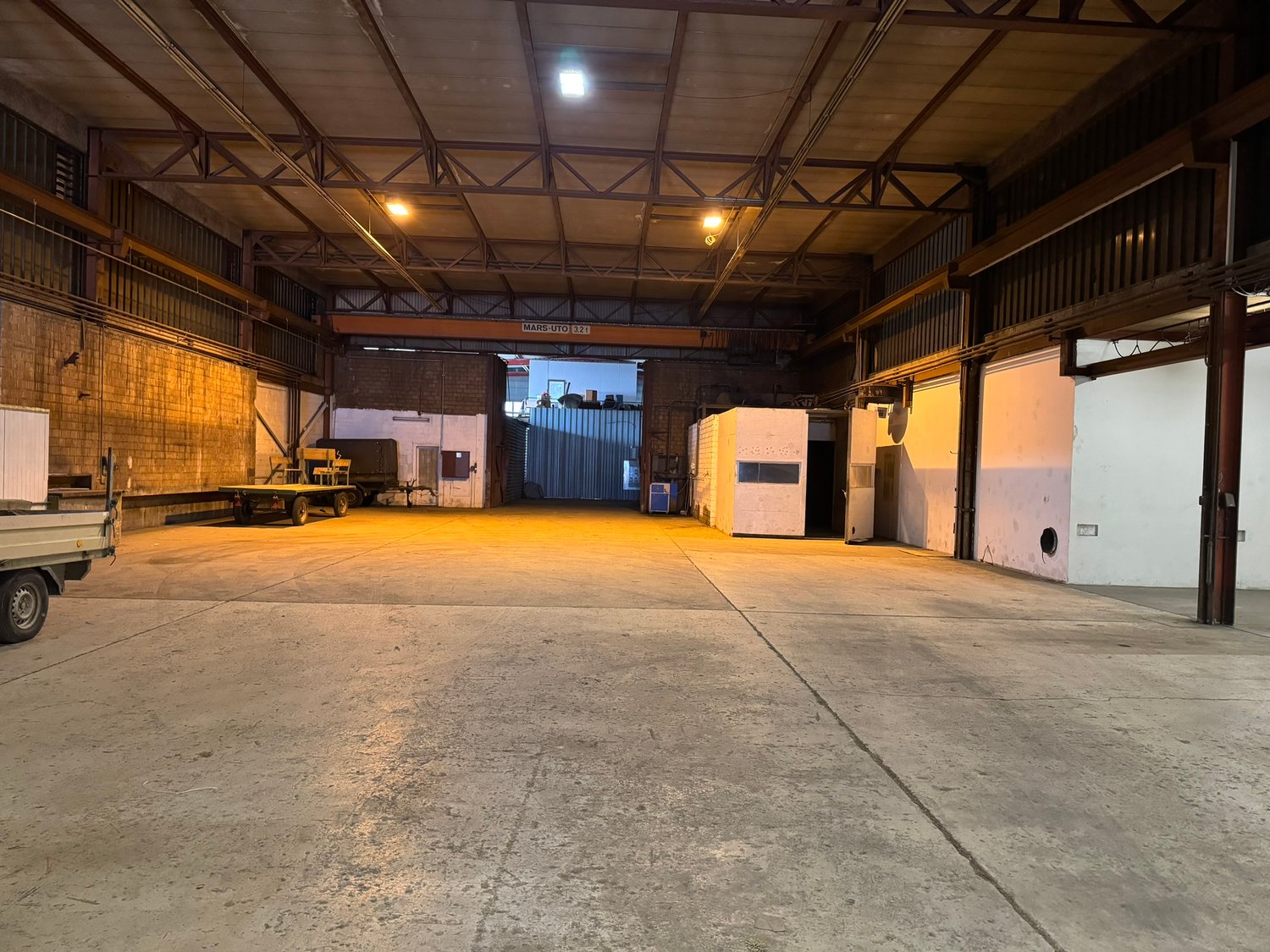 large warehouse with high ceilings, open space, brick walls, metal racks, 2 white doors, a truck with trailer parked at the entrance, steel door at the end of the room