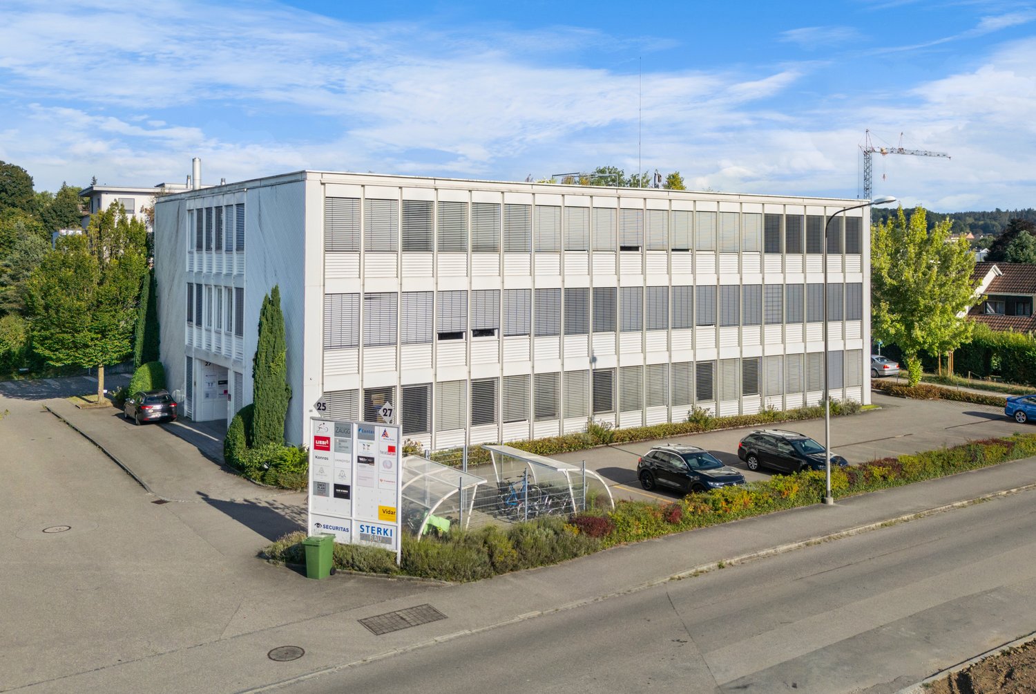 white office building with multiple windows, two stories, entrance, shrubs, parking area, bicycles parked under canopy