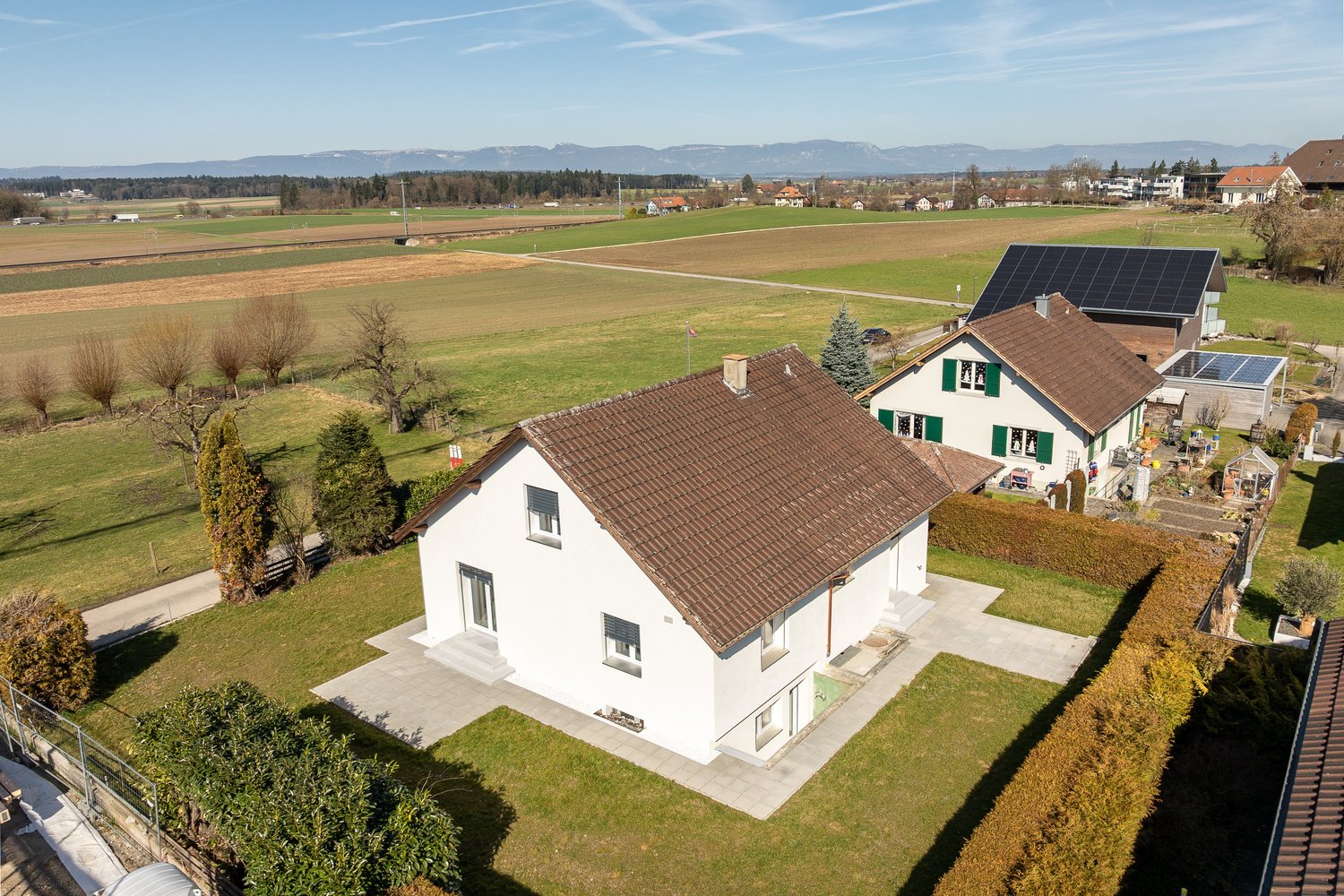 modern white house, brown roof, solar panels, large garden, driveway, surrounded by fields
