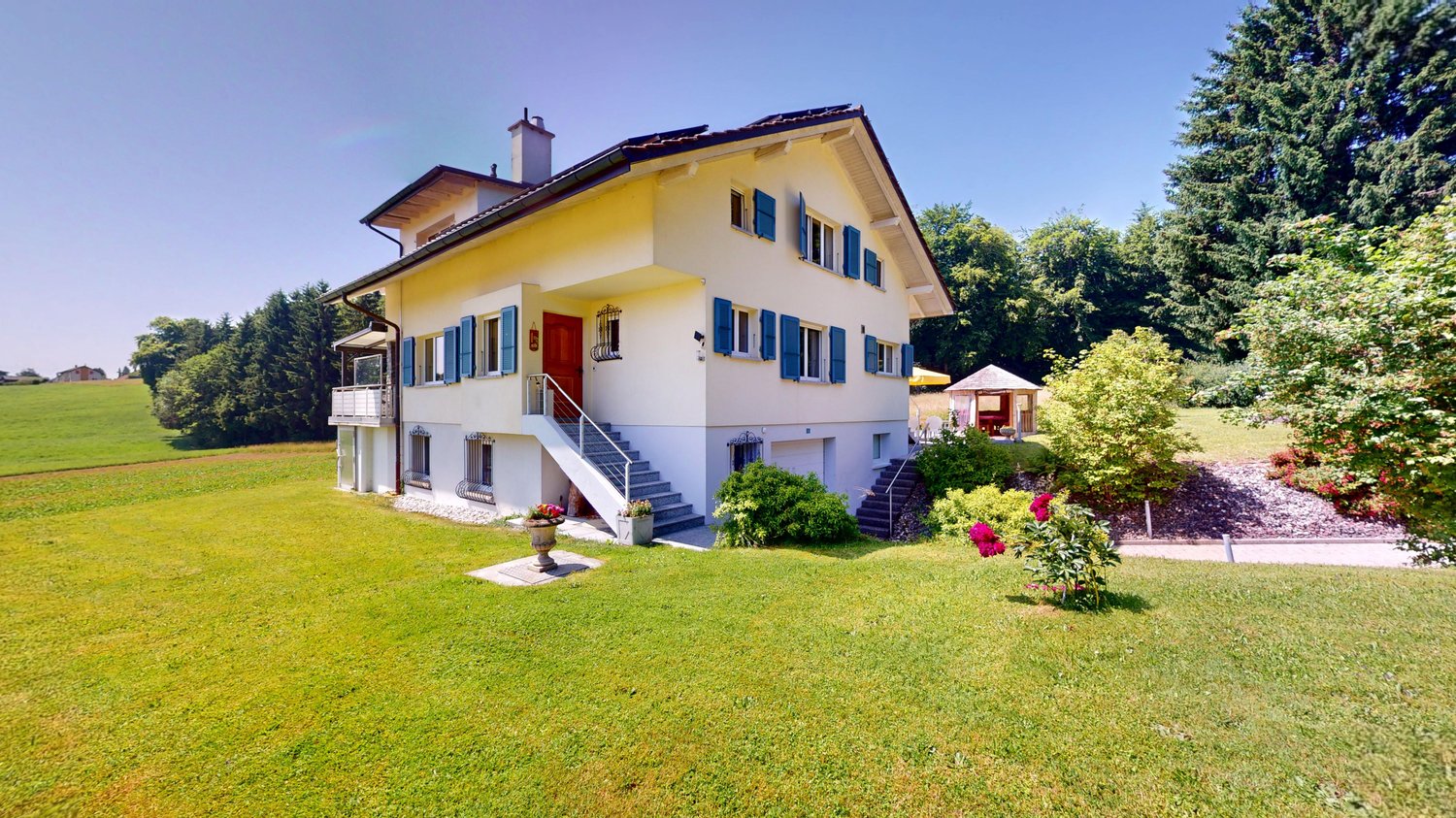 2 story house, yellow, white windows, blue shutters, red door, stairs to entrance, paved driveway, garden, flower pots, fence, small gazebo