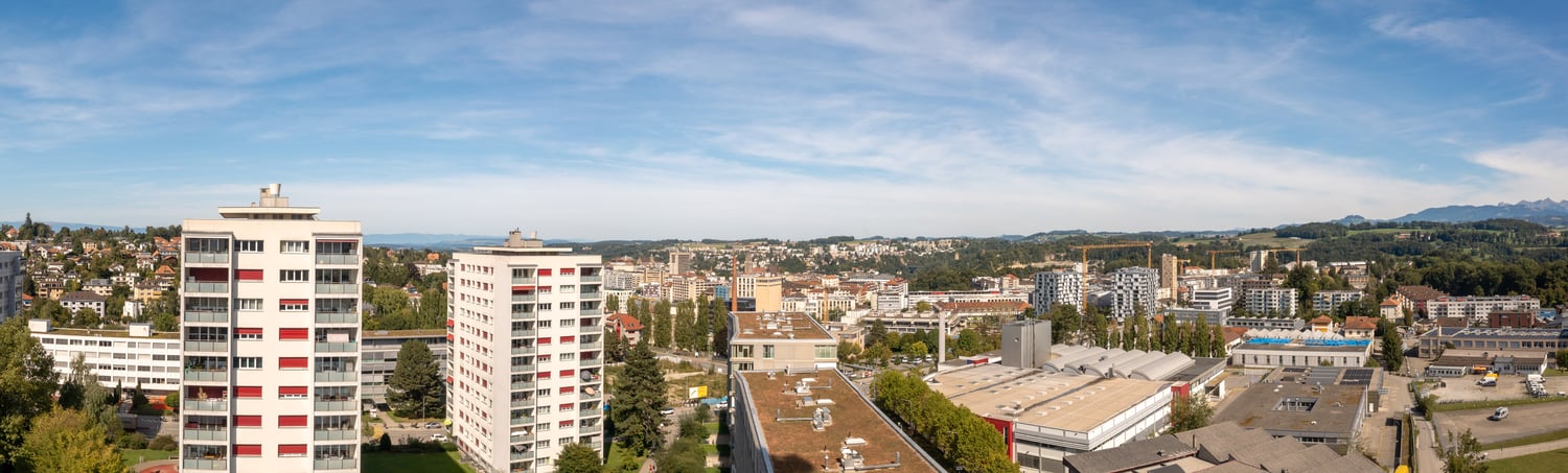 cityscape of a town with multiple buildings, trees, hills in the background