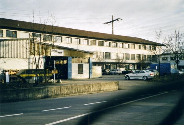A building with several windows, parked cars in front, street light pole, road.