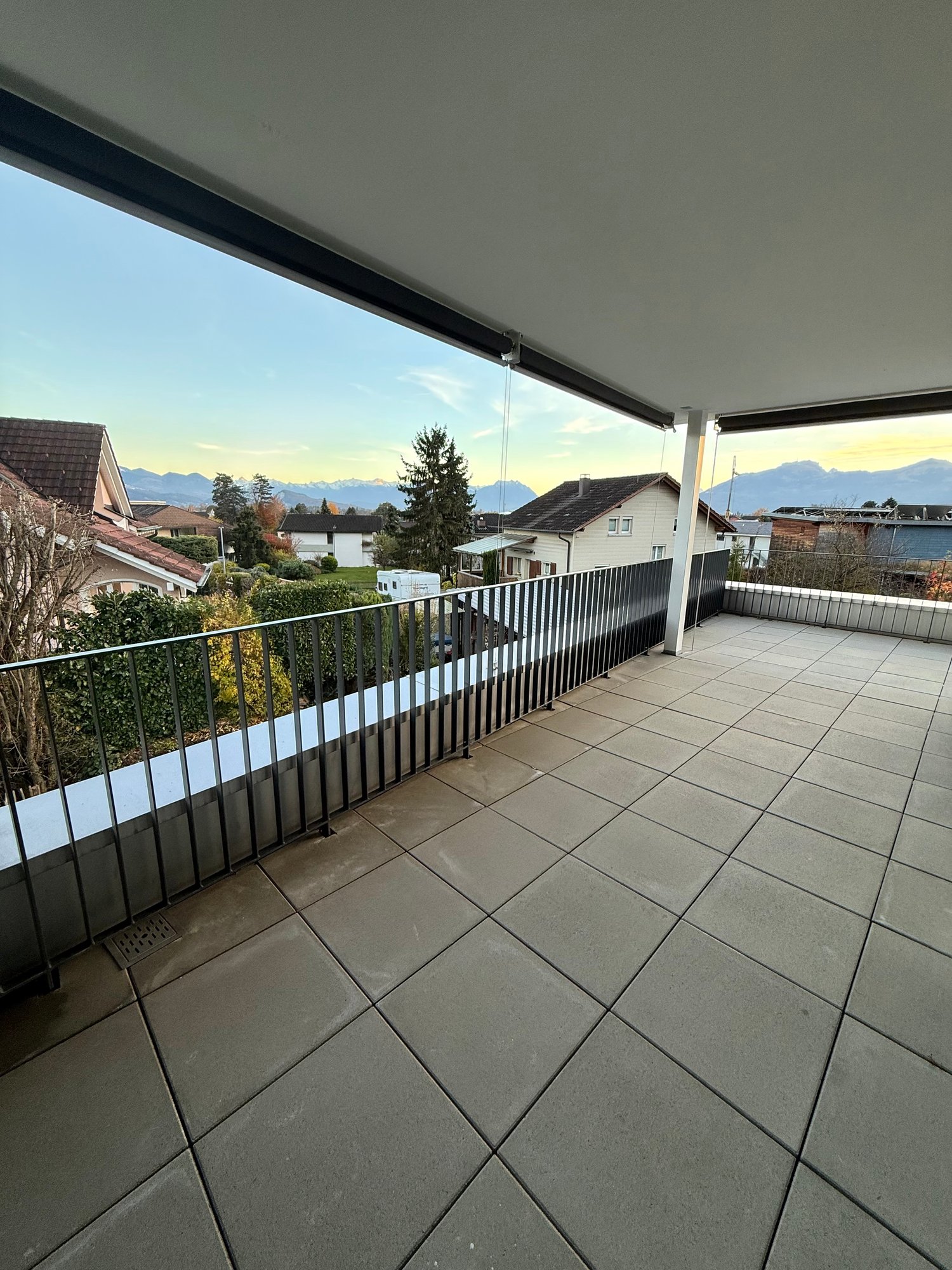 Tiled floor balcony with black railings, overlooking a landscape with mountains and houses
