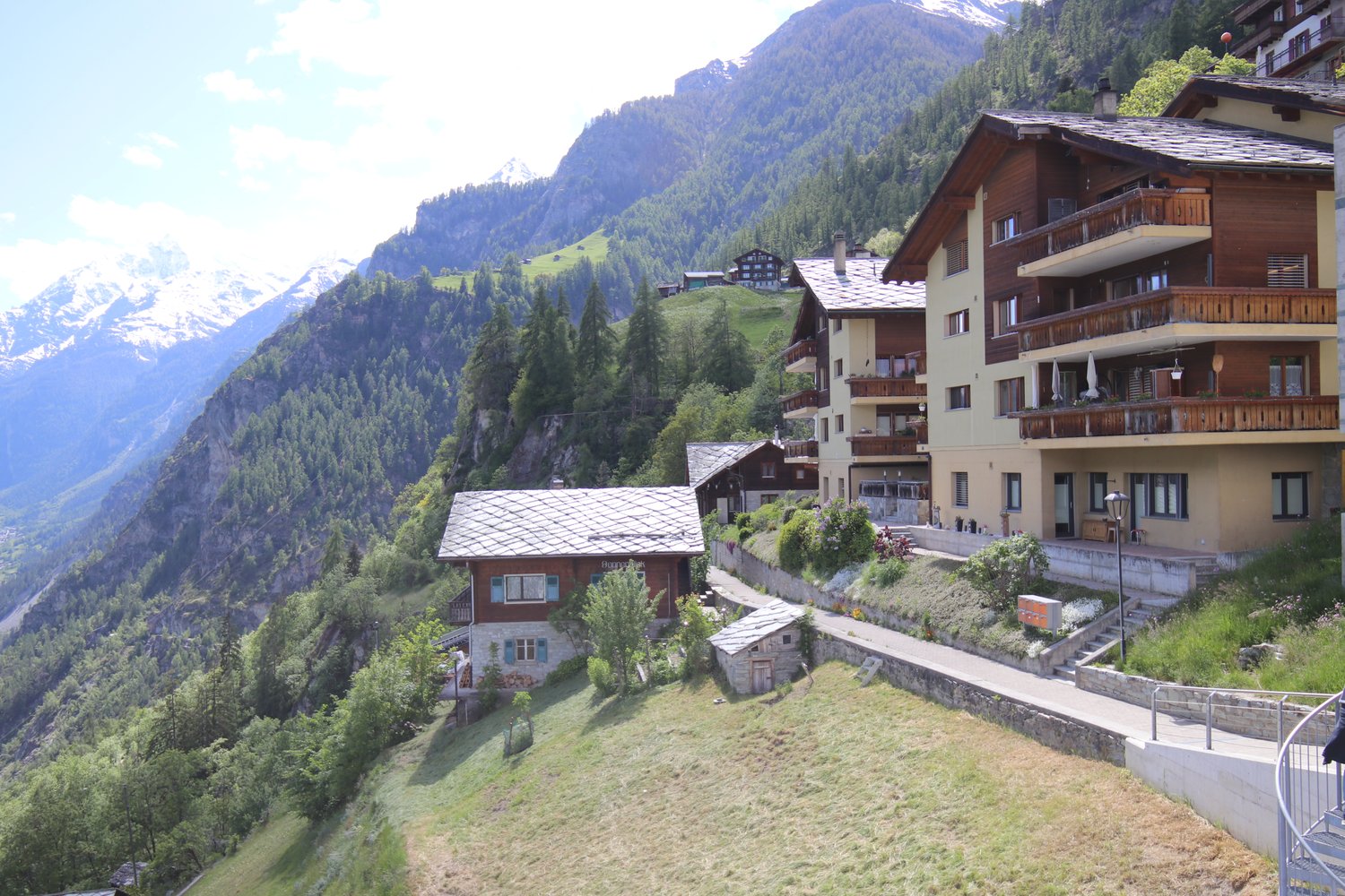 multiple wooden buildings, located on the slopes of a mountain, surrounded by greenery, offering a stunning panoramic view of the surrounding mountains