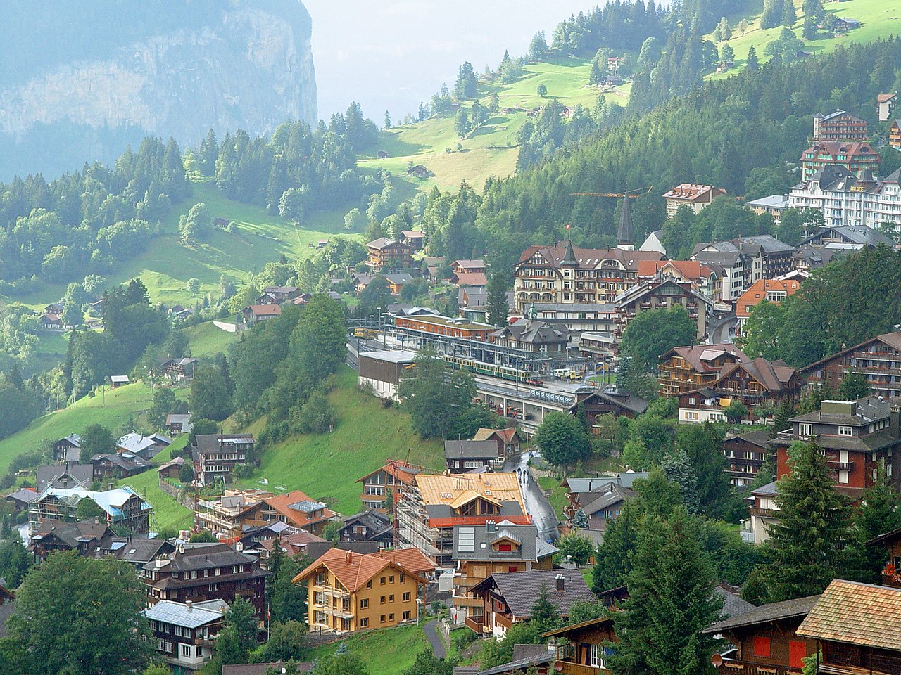 Mountain village with many houses, green hills, trees, and a mountain in the background