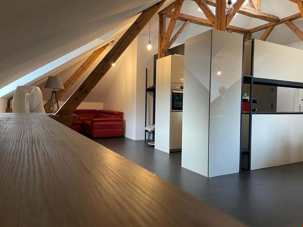 Exposed wooden beams, red couch, grey carpet, white kitchen, lamp, ceiling lamp, wooden table