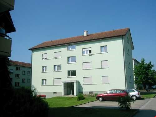 3 story apartment building, green exterior, brown roof, multiple windows, cars parked in front