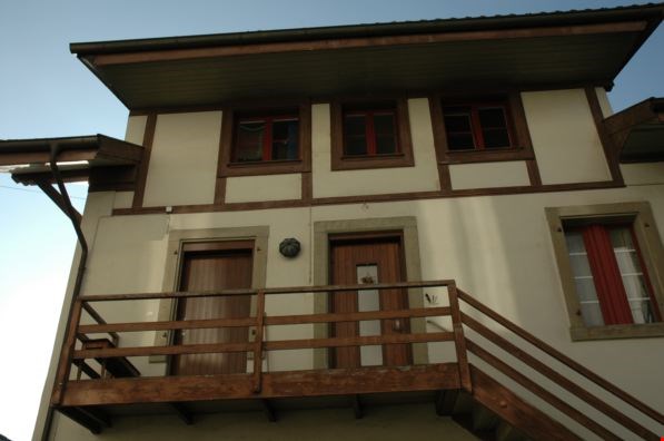 2 story house, beige and brown trim, wooden balcony, wooden doors, windows with red frames
