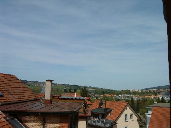 Aerial view of a neighborhood with multiple houses, brown roofs, chimneys, and a distant view of hills and buildings.