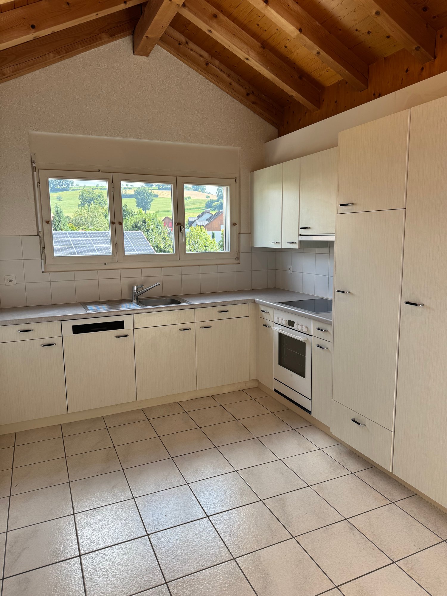 modern kitchen with white cabinets, tiled floor, granite countertop, sink, oven, dishwasher, and large windows with a view of the outdoor landscape.