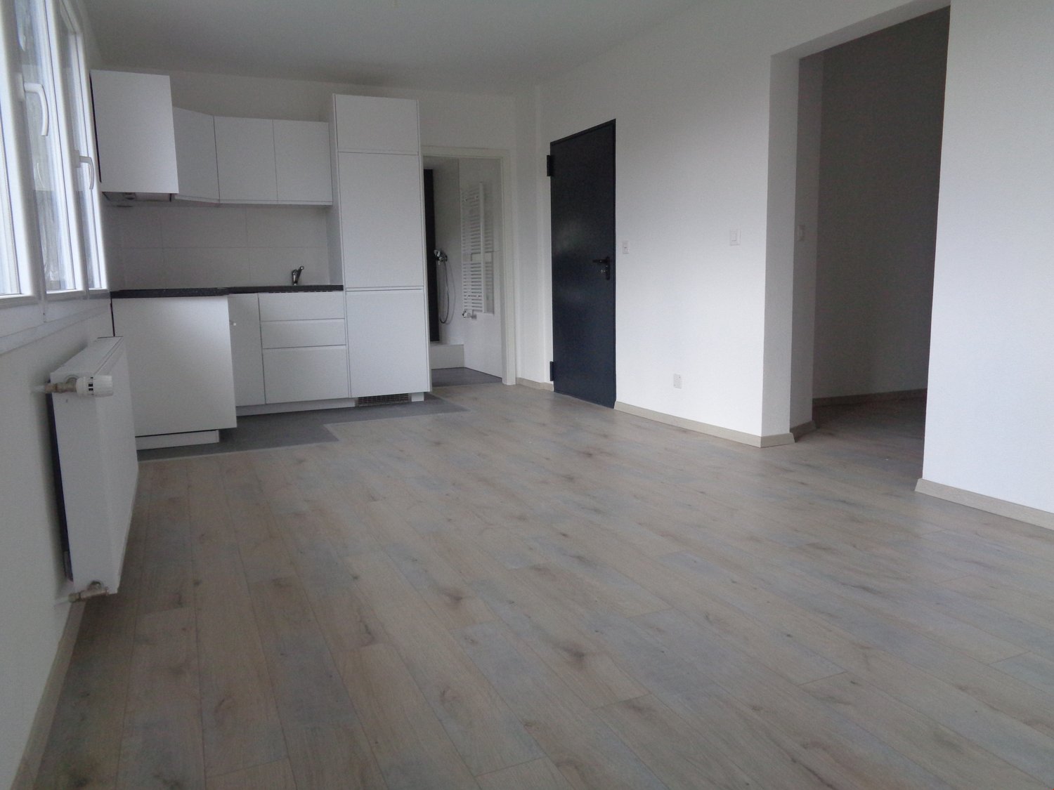 Modern kitchen with white cabinets, countertops, tiled floor, radiator, and faucet