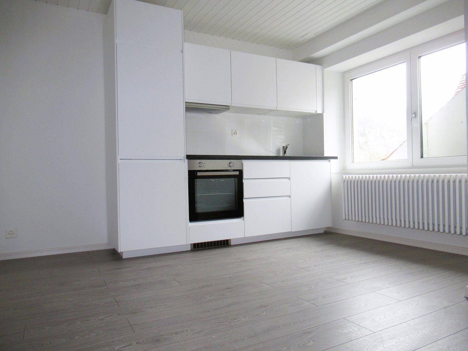 modern kitchen with white cabinets, black oven, white tiled backsplash, white radiator, wooden floor