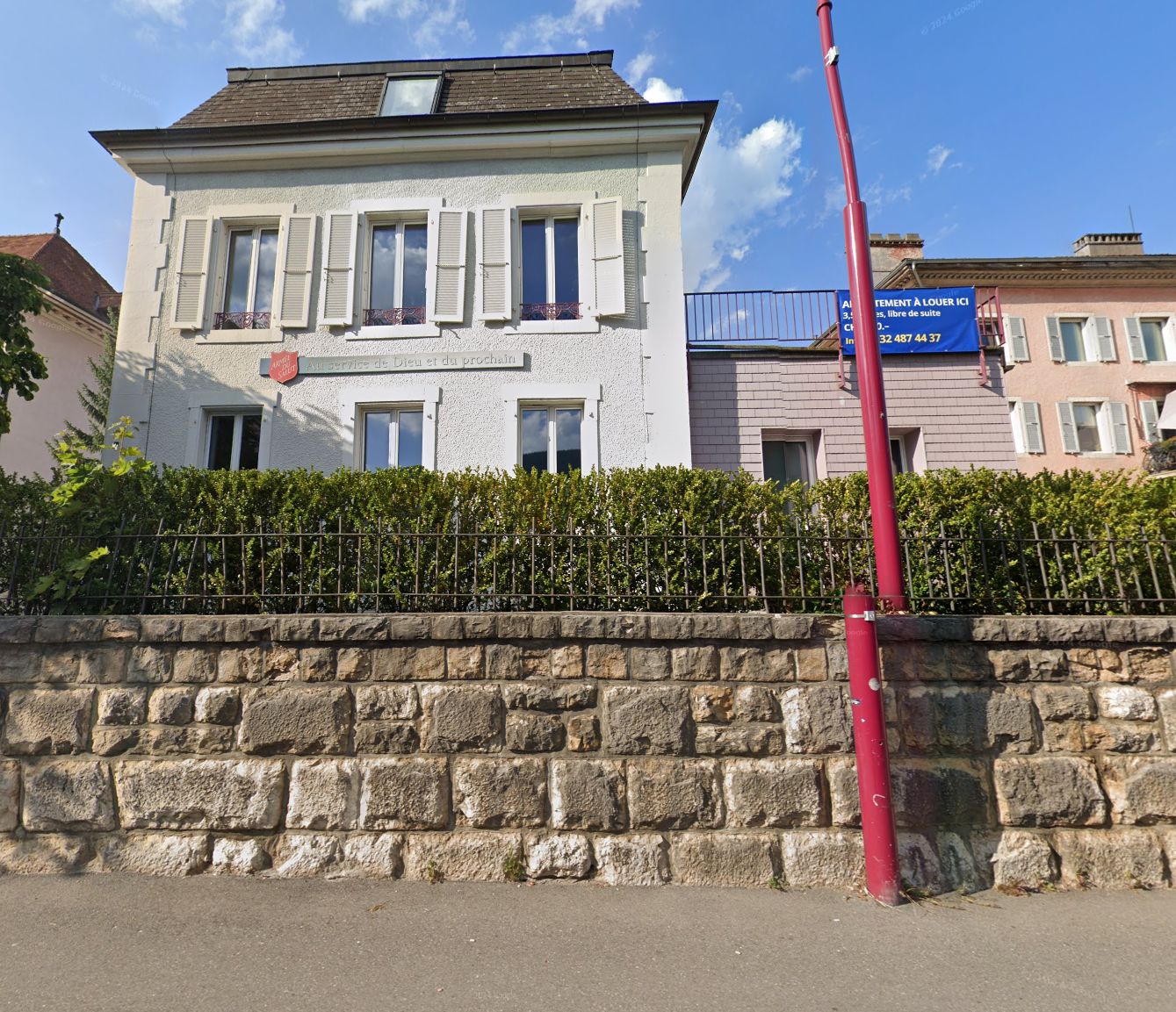 3 story white stucco house, brown roof, white shutters, brick wall, hedges