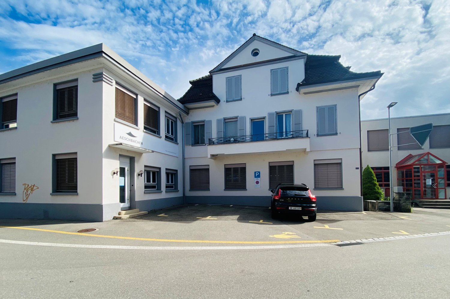 white building, three stories, parking lot, car parked in front