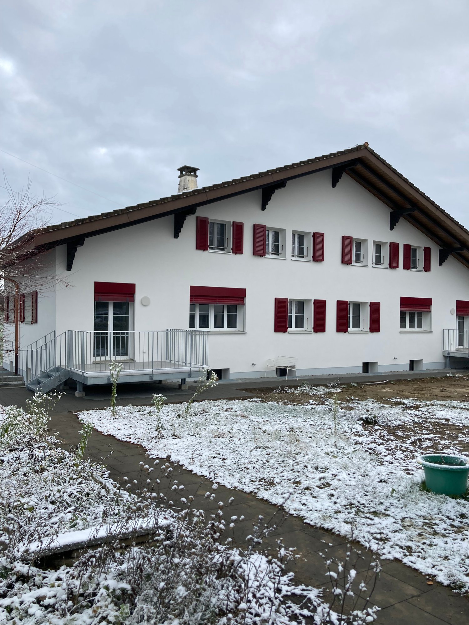 white house, red shutters, sloped roof, covered porch, metal railing, front garden, chimney