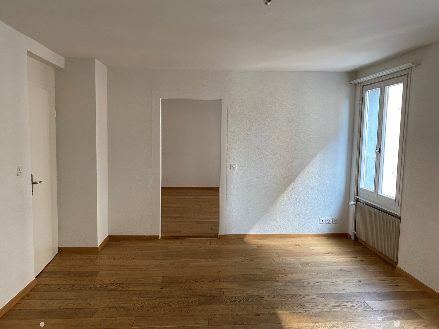 empty room, wooden floor, white walls, door, window, radiator
