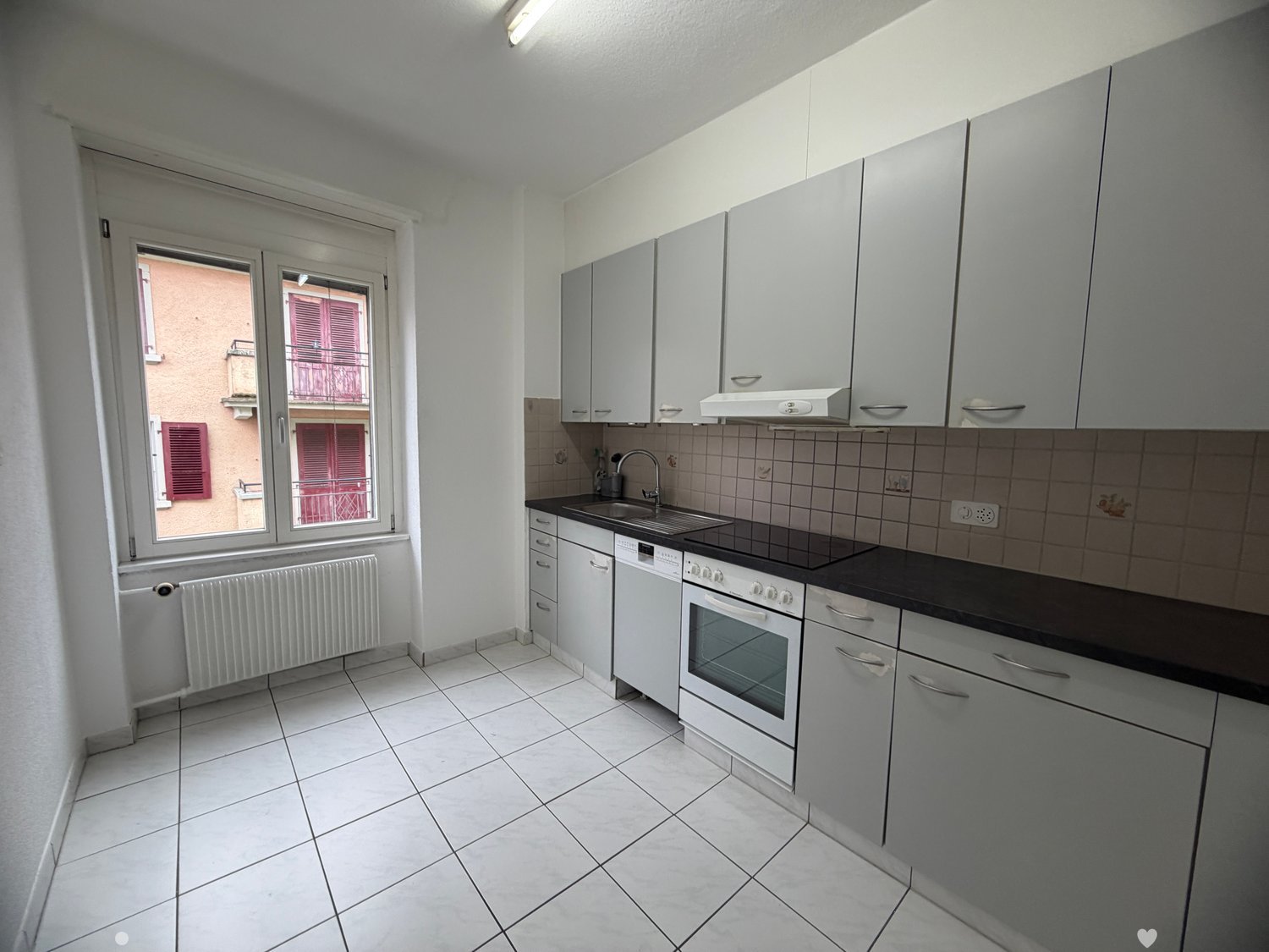 modern kitchen with white tiles, white cabinets, black countertops, white appliances, window with view to the outside