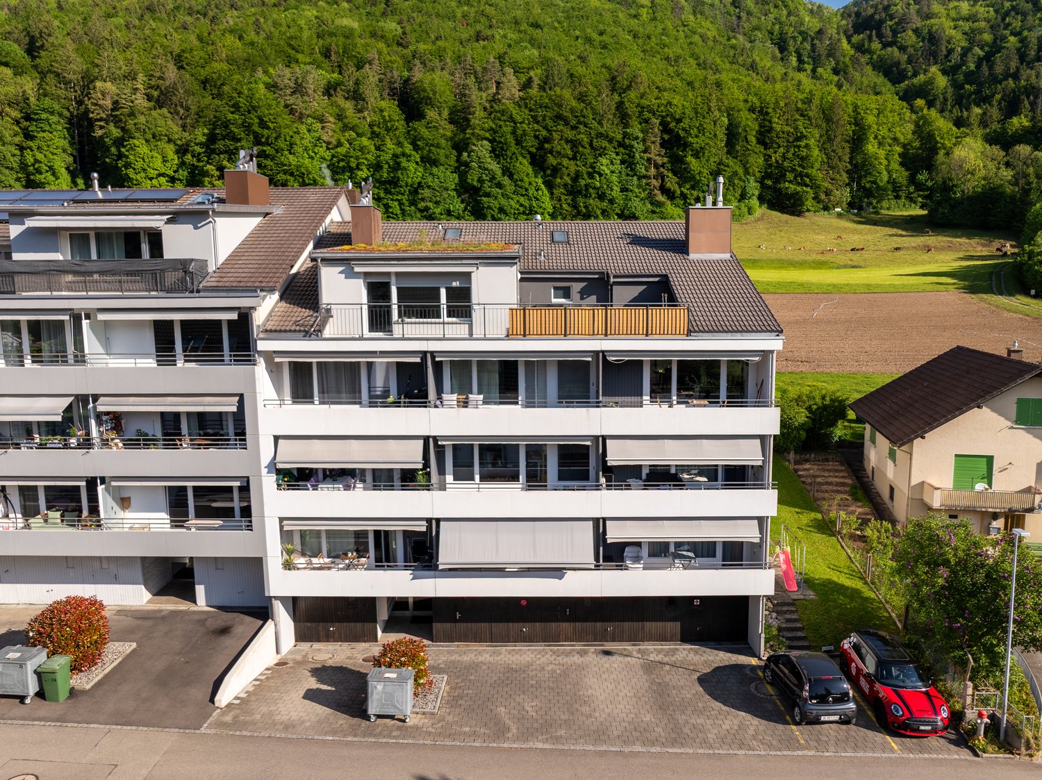 A multi-story building with solar panels on the roof, balconies, and a parking area in front.