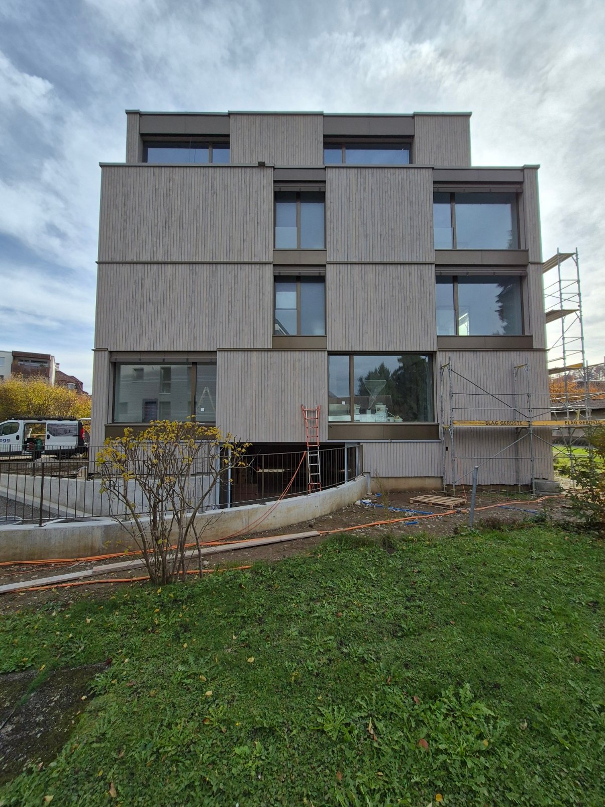 multi-story building, concrete and glass structure, 4 windows per floor, scaffolding on the right side, a vehicle parked in front