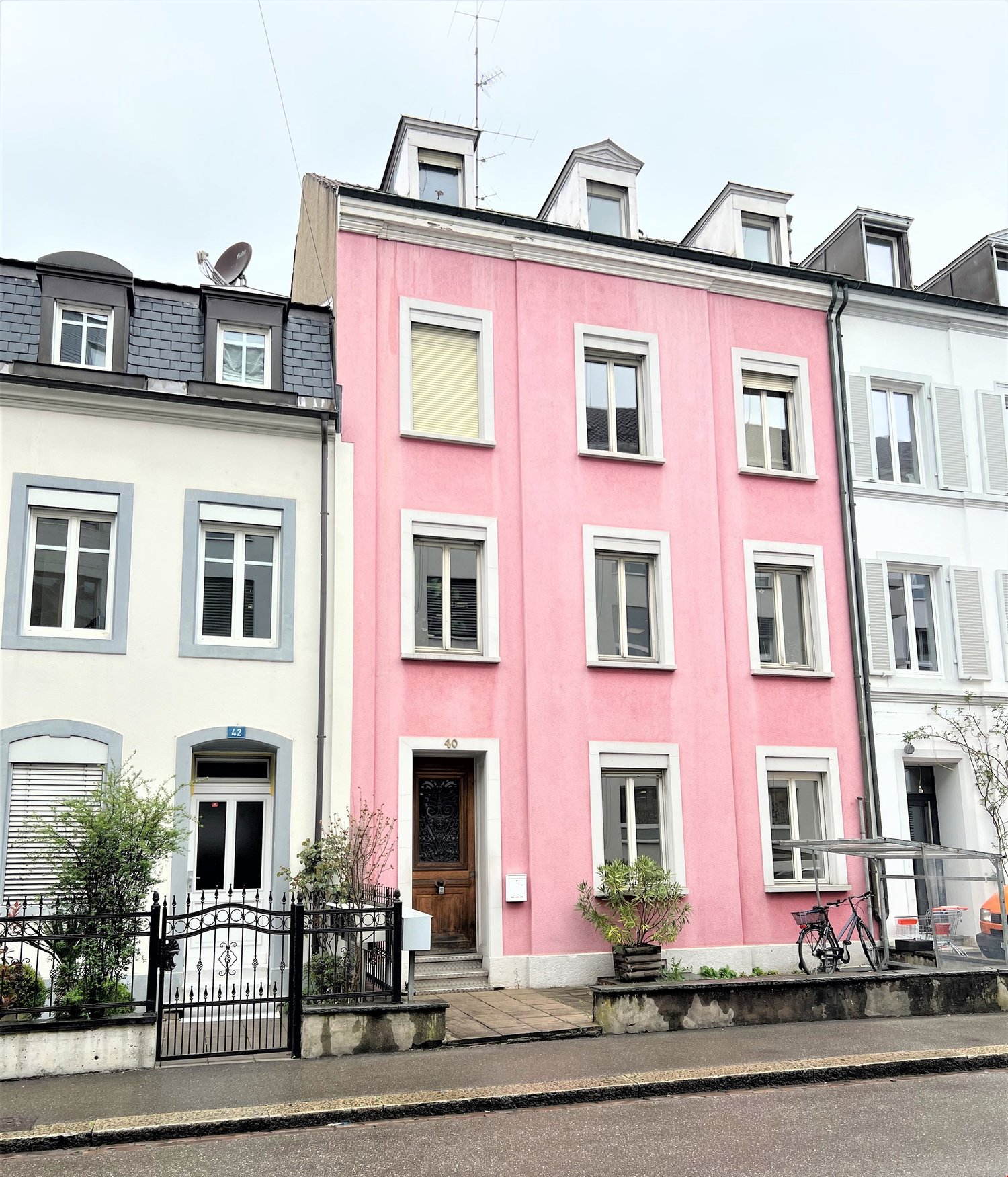 3 story building, pink facade, 6 windows on the front side, black fence, door