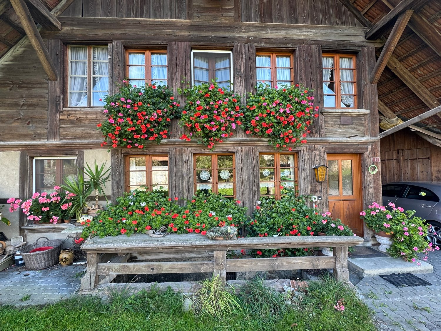 Traditional wooden house with flower boxes, wooden door, wooden bench, car parked in front