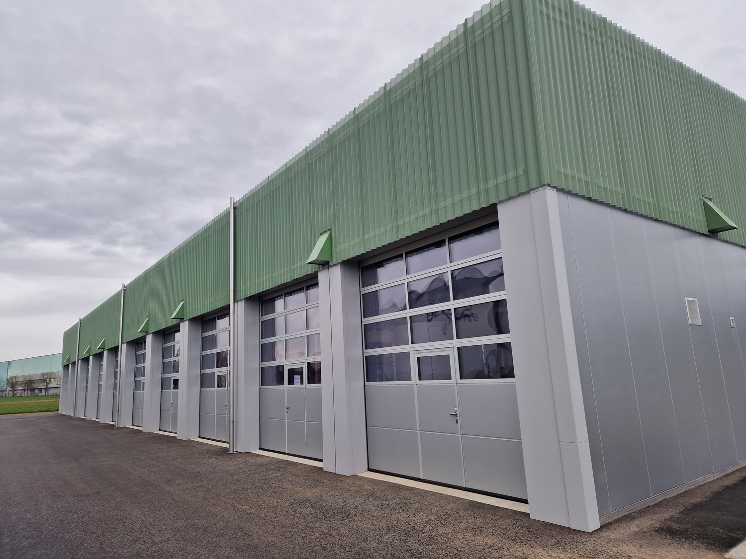 Warehouse, large garage doors, large windows, green and grey exterior, multiple entrances