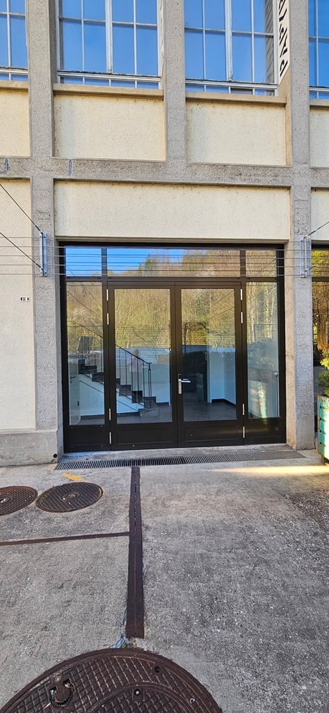 Modern building with glass doors and windows, concrete structure, staircase visible through the glass