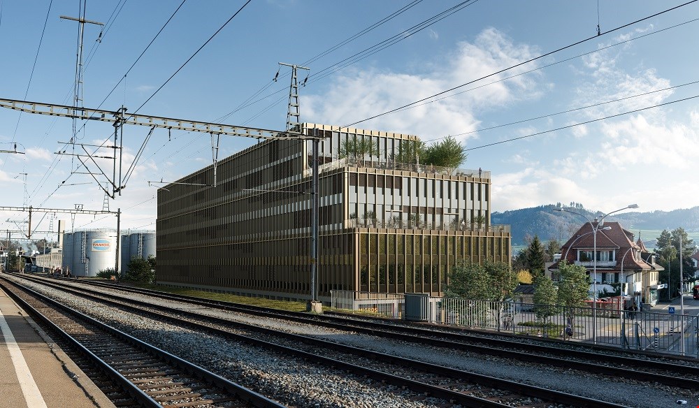 Modern office building with glass facade, located near a railway track, surrounded by trees and a house