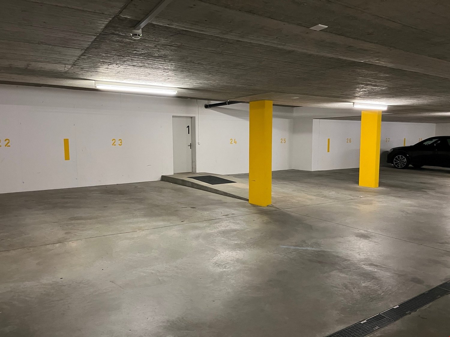underground parking lot, white walls, yellow pillars, numbered parking spots, a black car parked in spot 27