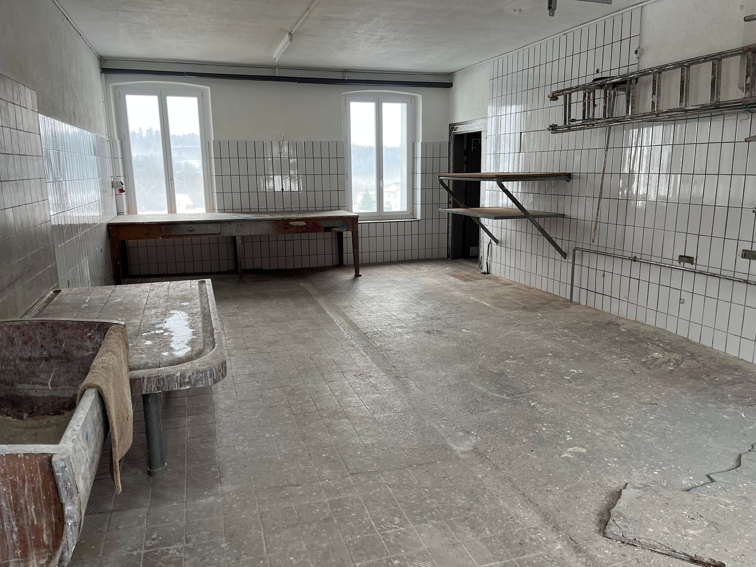 empty room, white tiles, concrete floor, wooden table, sink, ladder, 2 windows