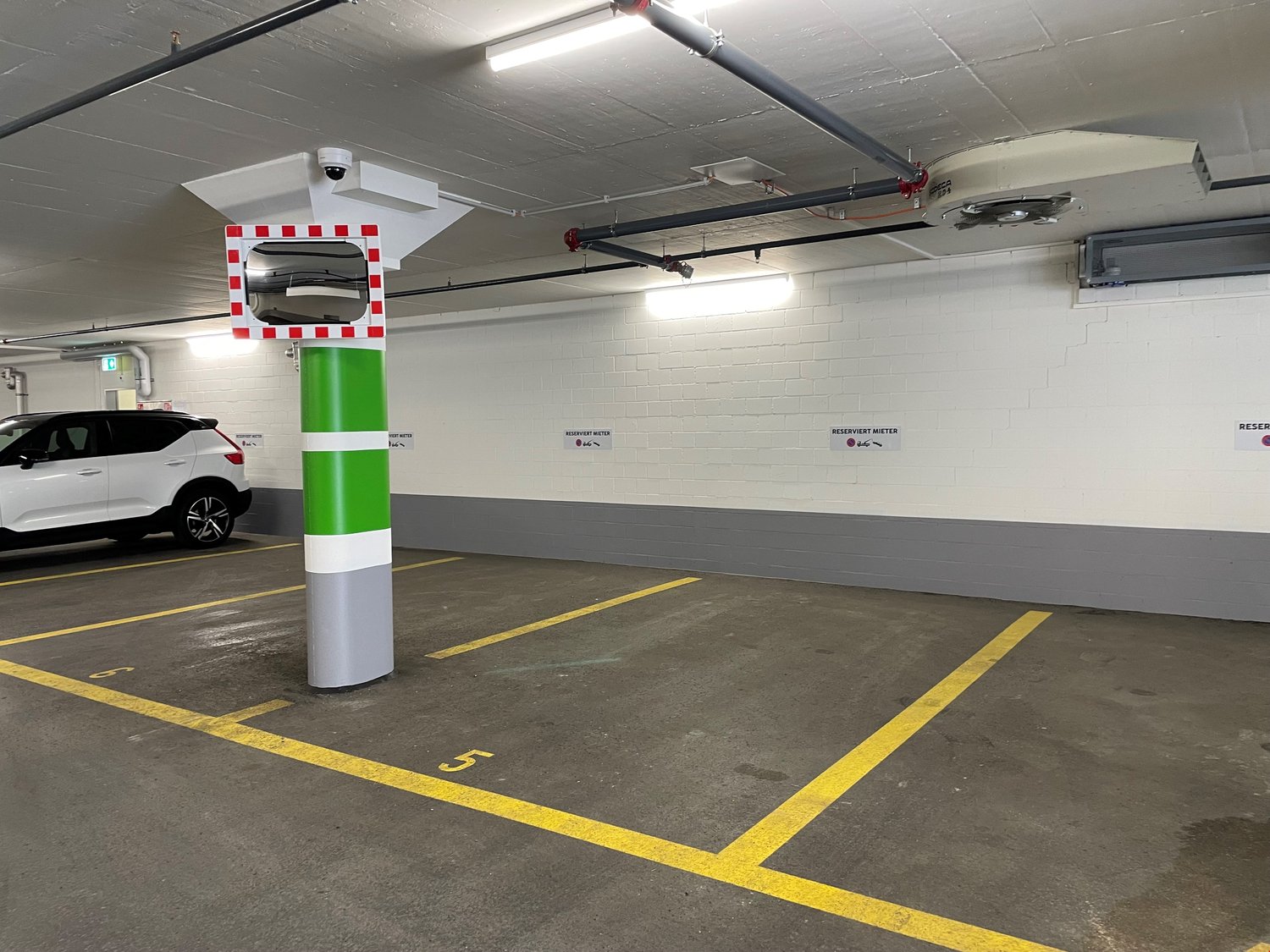 underground parking area with white walls, yellow and gray parking lines, a central pillar with a camera, a car parked