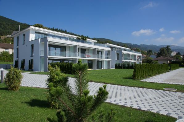 Modern two-story apartment building, white exterior, glass balconies, landscaped front yard