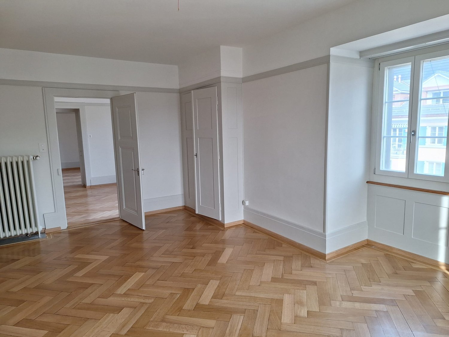empty room, wooden parquet floor, white walls, open door, radiator, windows