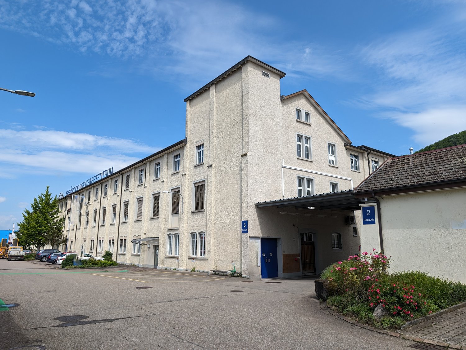 3-story office building, beige exterior, multiple windows, blue door, parking lot in front, green vegetation, street light