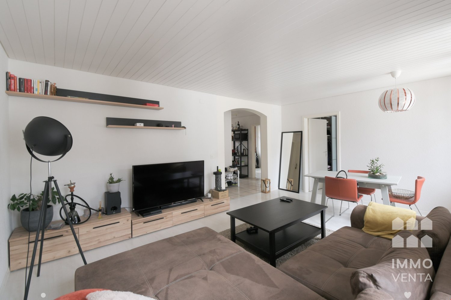 white floor, white walls, modern interior, TV on a stand, couch, coffee table, dining area, mirror on the wall