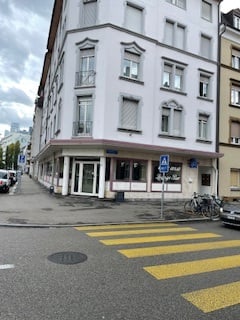 A white building with multiple windows and balconies, located on a street with parked cars and bicycles.