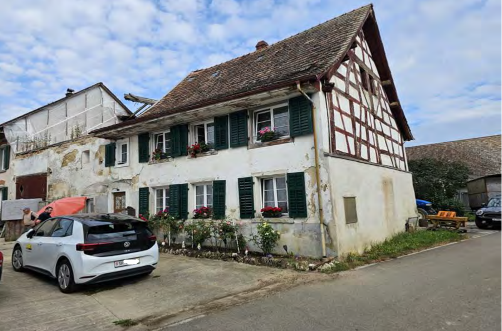2 story house, white paint, brown roof, green shutters, plants in front, cars parked