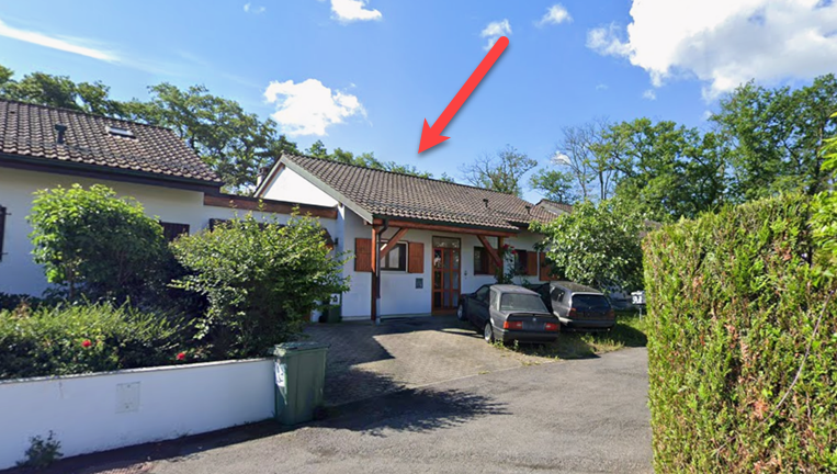 Detached house, brown roof, white walls, brown shutters, driveway, 2 cars parked, green trash bin, hedge