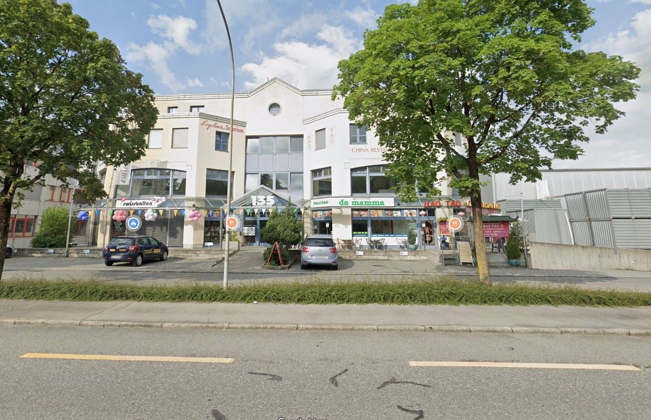 Buildings with restaurants, 2 cars parked, trees in front, road with lane markings